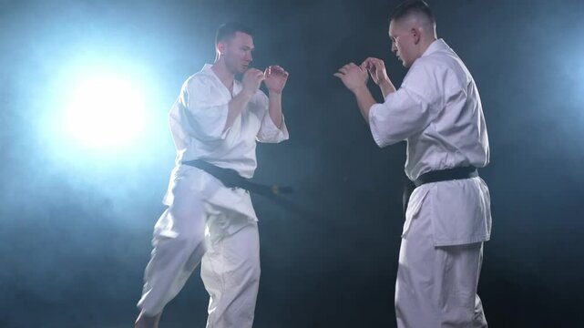 Martial arts masters on dark background. Strong man fighters in white kimono for karate martial arts fighting training in black gym. Karate fighters training punches kicks practicing fight sparring