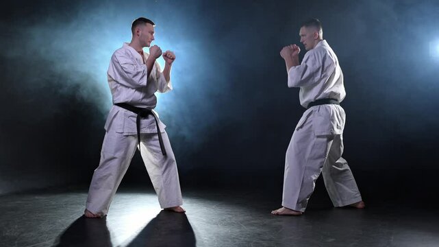 Martial arts masters on dark background. Strong man fighters in white kimono for karate martial arts fighting training in black gym. Karate fighters training punches kicks practicing fight sparring