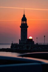 sunset over a lighthouse with a clock tower in the middle of the ocean