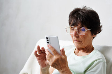 Senior woman with eyeglasses looking at mobile phone, scroll images, messages, texting for networking on app for social media.