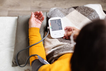Senior woman measuring her blood pressure. Retired uses medicine digital device tonometer for...