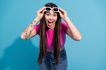 Happy young woman in a pink casual top striking a playful pose while holding sunglasses on a vibrant blue background