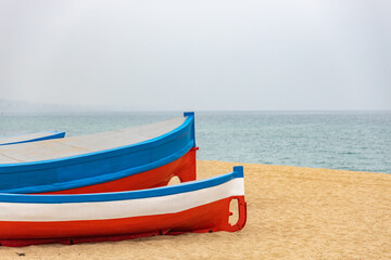 Fototapeta premium Two boats are sitting on the beach, one blue and one red