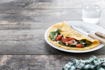 Stuffed omelette with tomatoes and spinach on wooden table. Copy space