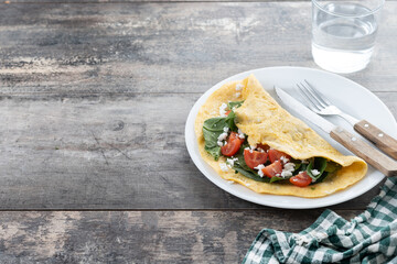 Stuffed omelette with tomatoes and spinach on wooden table. Copy space