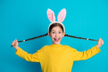 Joyful young girl with braided hair wearing bunny ears on blue background, expressing happiness and playfulness
