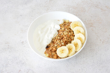Granola with yogurt and sliced bananas in a white bowl