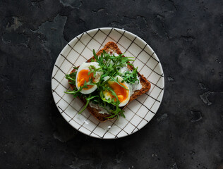 Sandwich with cream cheese, boiled egg, arugula on a dark background