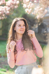 Fototapeta premium Stylish young woman standing under blooming magnolia trees in a Prague park. A modern take on fashion, nature, and city vibes in spring