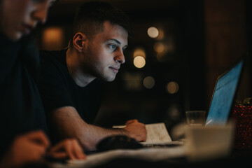 A young adult man intensely concentrating on a laptop, set in dim lighting indoors. The scene conveys dedication, focus, and the ambience of working in a serene and quiet setting during the night.