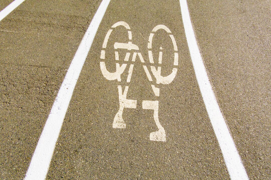 A cycle route in a public park, white painted outline of a bicycle, cycling lane on a pedestrian pathway.