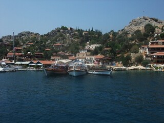 Coastal village with moored wooden boats along the shore, traditional houses and rocky hills under...