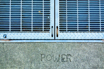 A metal grille over a power utility vault on a wall, the word Power embossed in stone.