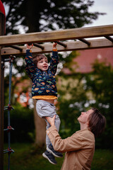 Obraz premium Parent Helping Child Hang on Monkey Bars at Playground