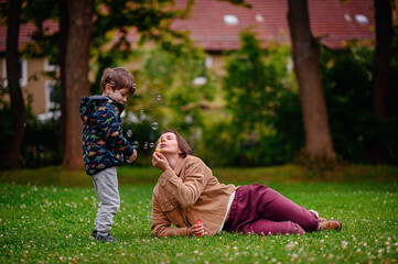 Fototapeta premium Child Playing Near Parent Blowing Bubbles in Park