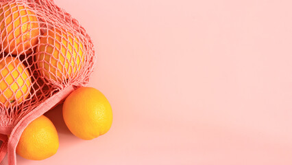 Fresh ripe oranges on net bag. Pastel pink background with space for text.