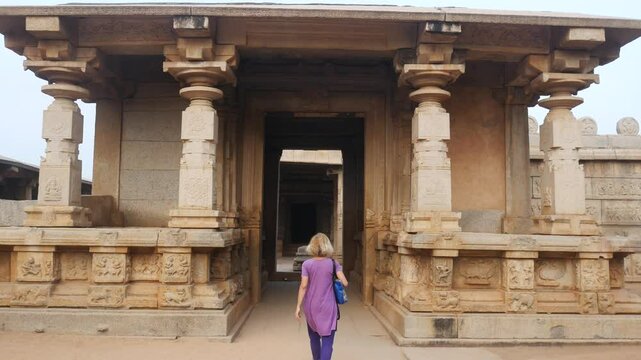Woman exploring amazing temple complex at Hampi, world famous unesco site. Tourist walking among ruins stone walls gateways in Karnataka, India