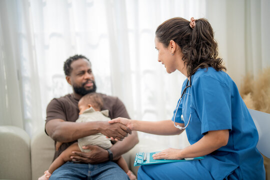 Healthcare professional shakes hands with a father holding his baby in a clinic during a routine checkup