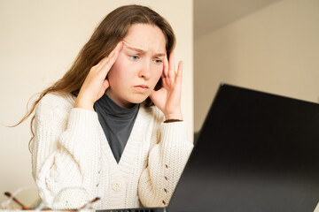 A young puzzled woman looking at a laptop screen at home. Confused female freelancer annoyed by...