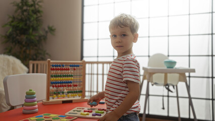 Young blond boy playing with colorful educational toys indoors in a well-lit kindergarten setting