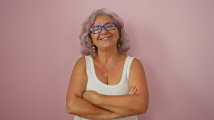 Hispanic woman with grey hair and glasses smiling confidently with arms crossed, standing against...
