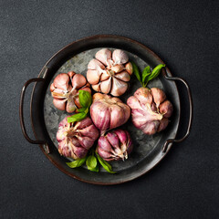 Metal tray with fresh organic garlic. Top view. On a black background. Minimalist photo.