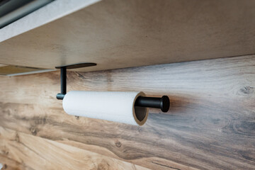 A roll of paper towels is hanging from a paper towel holder on a wooden wall