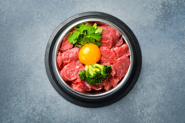 Food for dogs. Metal bowl of fresh meat with vegetables and egg yolk. Top view.