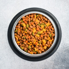 Pet bowl with dry food on a gray textured background. Studio photo.