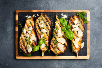 Baked eggplant with cheese and spices on a slate plate. Grilled vegetables. On a gray concrete background.