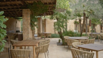 Blurred outdoor restaurant terrace featuring wicker chairs and tables under a vine-covered pergola with mediterranean ambiance.