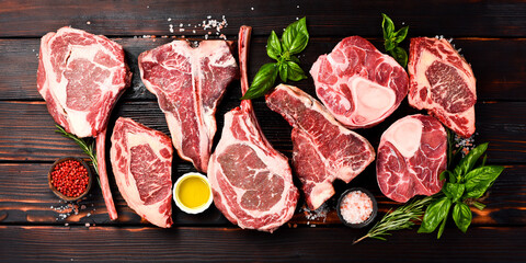 Variety of raw beef meat steaks for grilling with seasoning: Tomahawk steak, Ribeye, Ossobuco and...