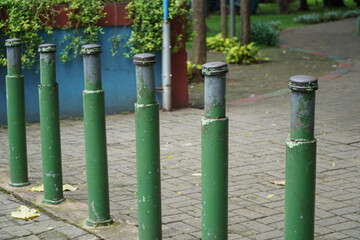 Fototapeta premium Row of Green Metal Posts in Urban Park Surrounded by Lush Foliage and Paved Pathway