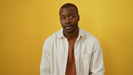 Obraz premium Young african american man isolated against a vibrant yellow background in a casual white shirt