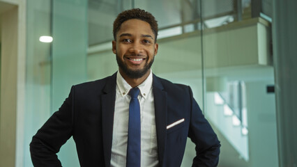 Fototapeta premium Young man smiling confidently in office workplace wearing a suit and tie, showcasing professionalism and business attire in an indoor corporate setting.