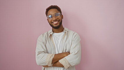Obraz premium Smiling young man with crossed arms stands against an isolated pink background, embodying happiness and confidence.