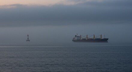 Obraz premium A cargo ship and lighthouse in dense fog at sea