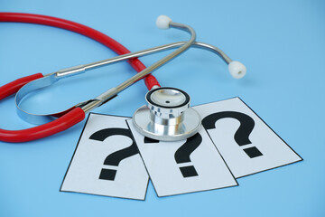 Red stethoscope on question marks on blue background close up.	