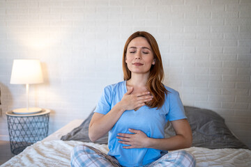 Serene woman practicing deep breathing exercise on bed