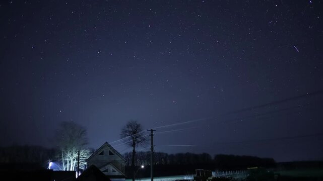 Meteors streaking across starry night sky above rural farmhouse