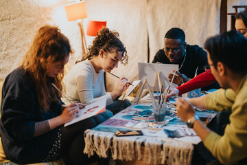 A group of diverse friends gathered in a cozy room while engaging in a creative art session, each...