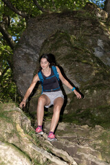 Obraz premium A young woman with a backpack carefully descends a rocky, forested trail surrounded by lush greenery and natural textures