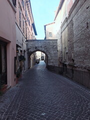 The ancient Arch of Drusus and Germanicus stands over a quiet cobblestone street in Spoleto, Italy. Historic Roman architecture in a charming urban setting.