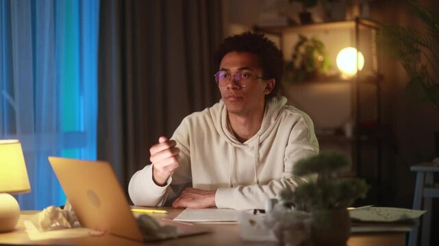 Young man sitting at laptop at home, suddenly getting new idea or insight, raising hand in realisation while working or thinking in cozy evening atmosphere, inspired by creative breakthrough