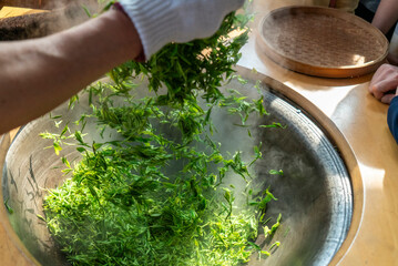 Traditional Chinese tea making techniques involve workers stir frying freshly picked green tea in iron pots