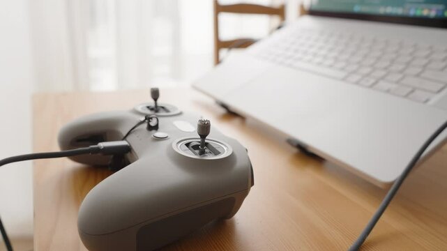 FPV Drone Joystick Controller with Cable Connected Sitting on Wooden Desk Next to Laptop in Natural Light, Side Angle, Setup Concept
