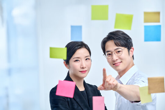 Two Young Professionals Discussing Plans and Strategies with Colorful Sticky Notes on a Glass Wall
