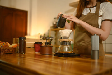 Close up of woman carefully pouring hot water into dripper to make fresh pour over coffee in a home kitchen