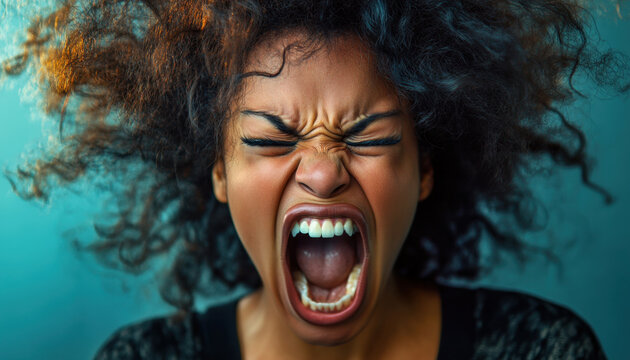 A Black woman with voluminous, wild hair shouts in frustration, showcasing raw emotion against a striking blue backdrop