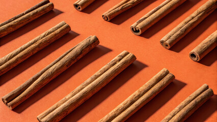 Cinnamon sticks arranged on vibrant orange background create minimalist spice concept, evoking warmth and flavor